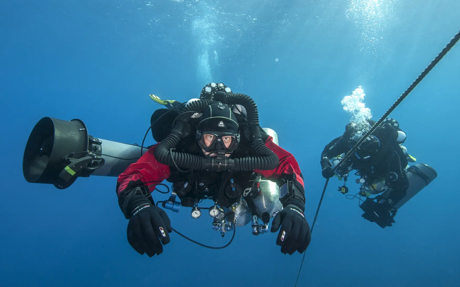 Technical diver in full gear with a Liberty closed-circuit rebreather, showing the oxygen cylinder, diluent cylinder, and breathing loop used for extended underwater dive time
